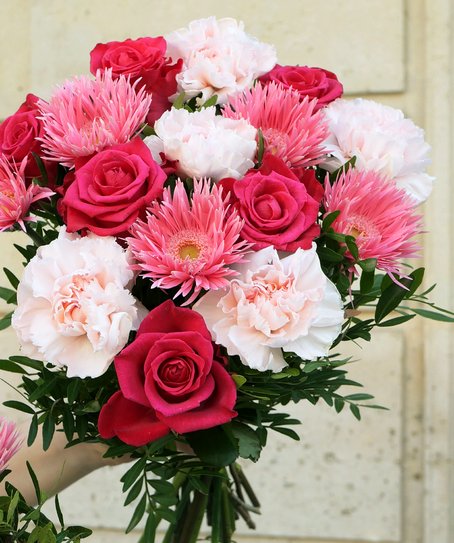 Main tient un bouquet de fleurs composé de germinis rose, oeillets rose pâle et roses cerise